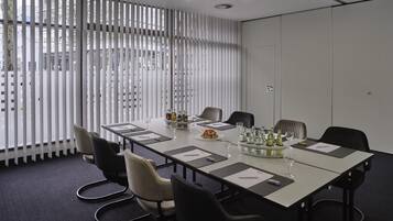 Ein Konferenzraum mit einem langen Tisch, Stühlen und einer Glastrennwand mit vertikalen Jalousien.