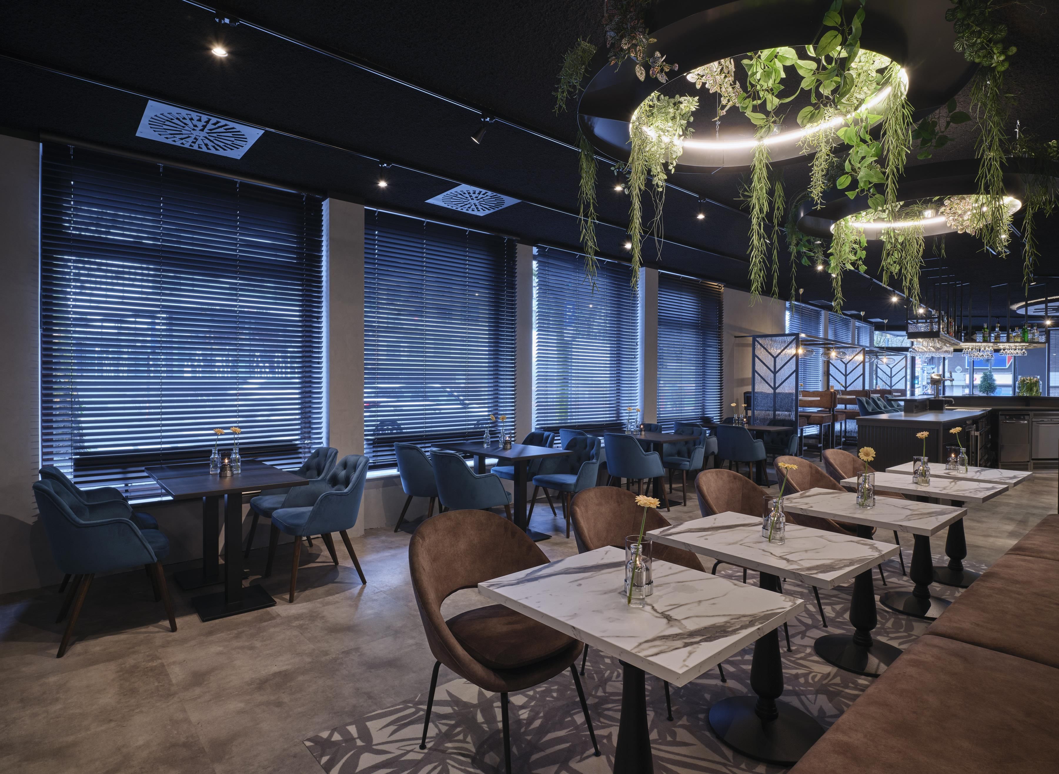 A restaurant interior with tables, chairs, hanging plants, and a bar area.