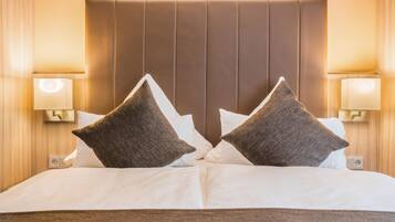 A hotel room with a large bed, two pillows, a headboard, bedside lamps, and a wall socket.