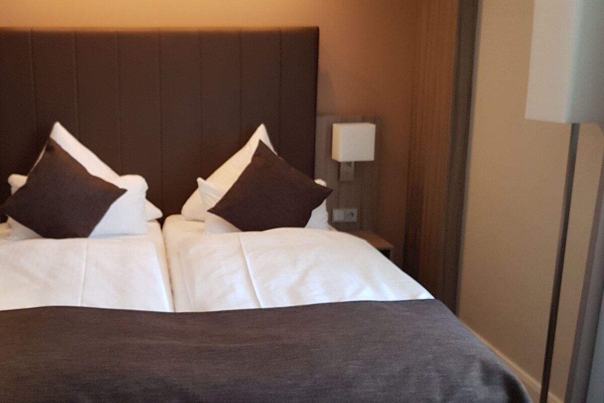 A hotel room with a large bed, two bedside lamps, and a dark headboard.