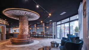 A modern interior with a central circular seating area, a bar with a unique ceiling design, and large windows offering a view of the street.