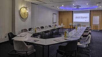 Een vergaderzaal met een lange tafel, stoelen, een scherm voor een beamer en een whiteboard.
