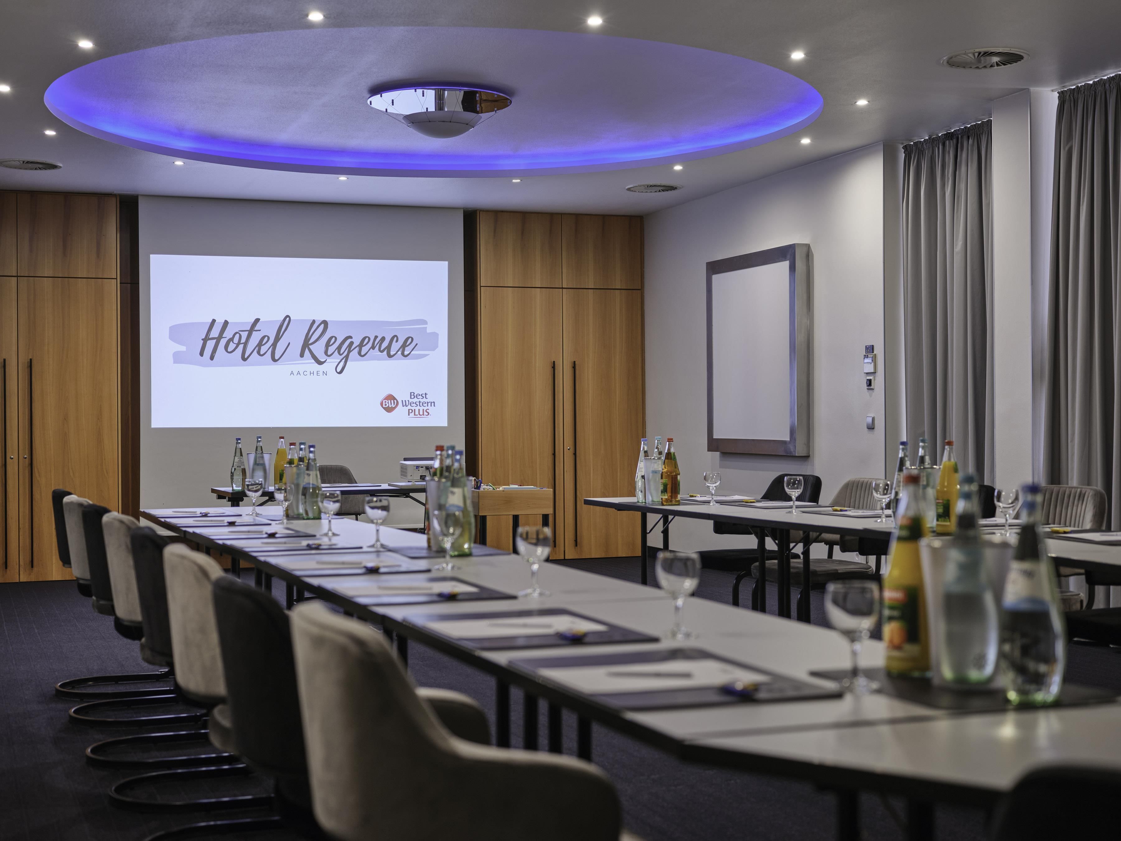 A conference room with a long table, chairs, and a presentation screen displaying 'Hotel Regency.'