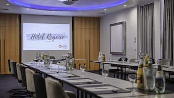 Un salón de conferencias con una larga mesa, sillas y una pantalla mostrando 'Hotel Regency'.
