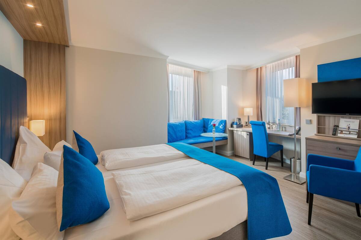 A hotel room with a bed, a desk, a chair, a TV, and a window.