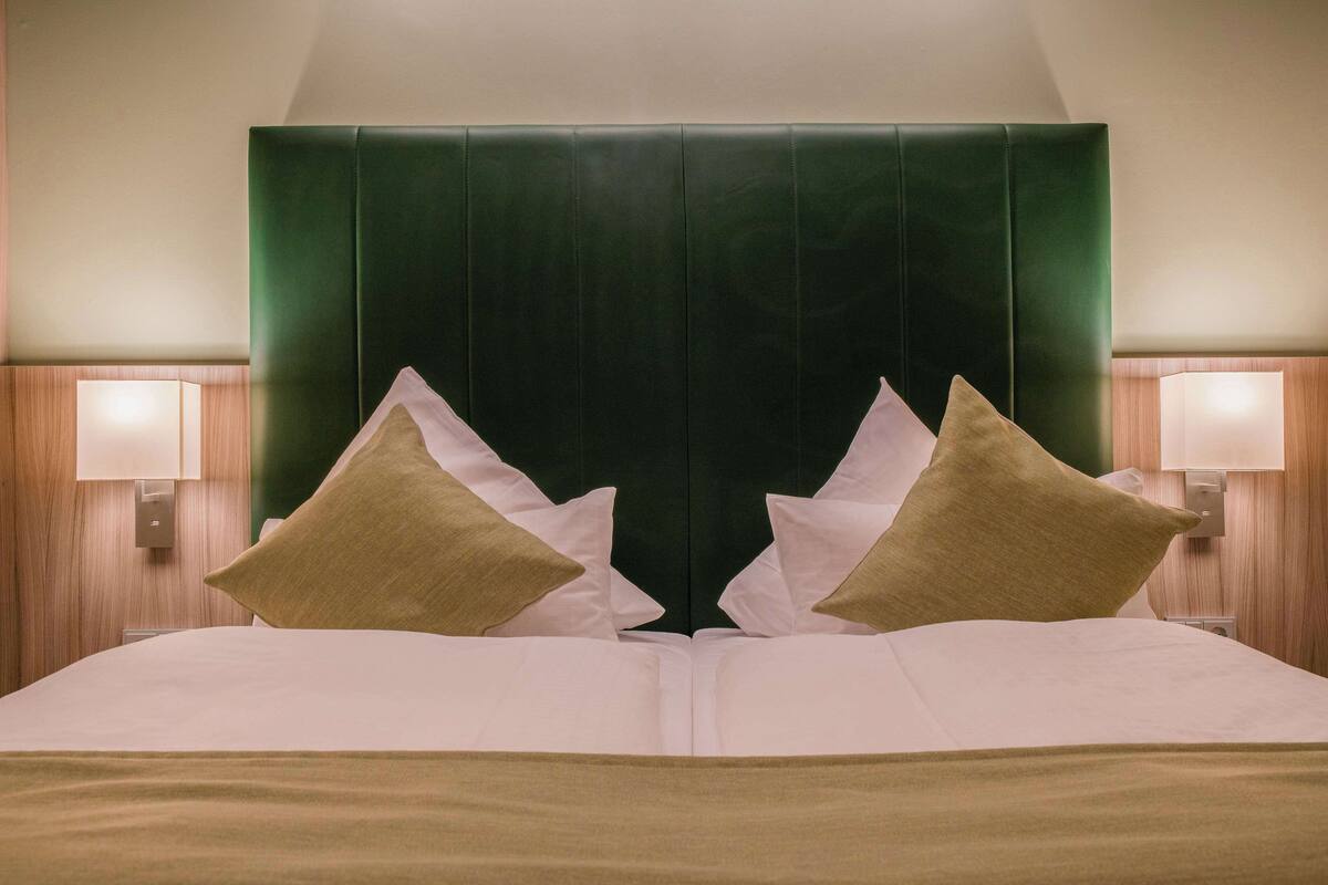 A hotel room with a large bed, two bedside lamps, and a green headboard.
