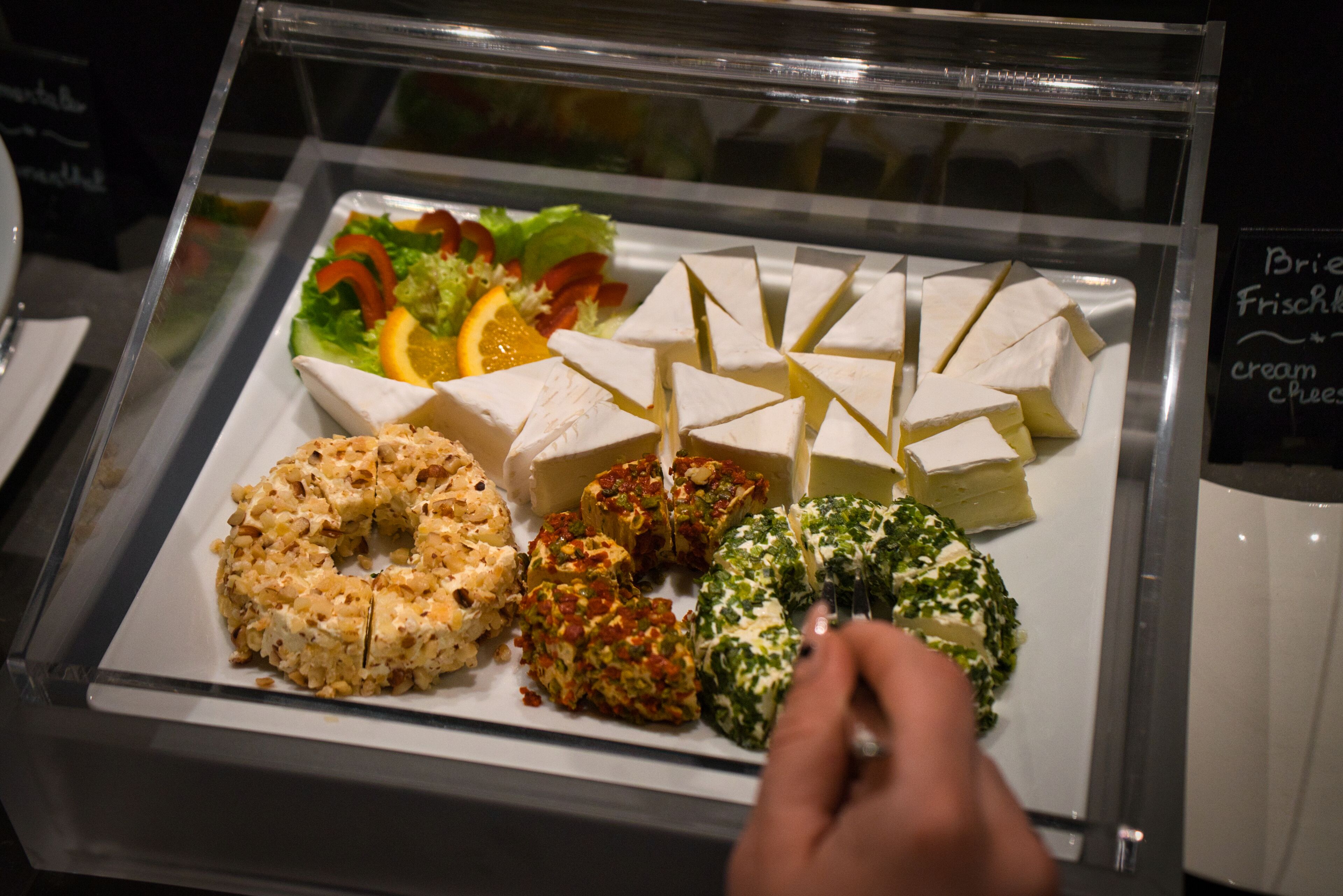 A food display with various cheeses, a salad, and a donut.
