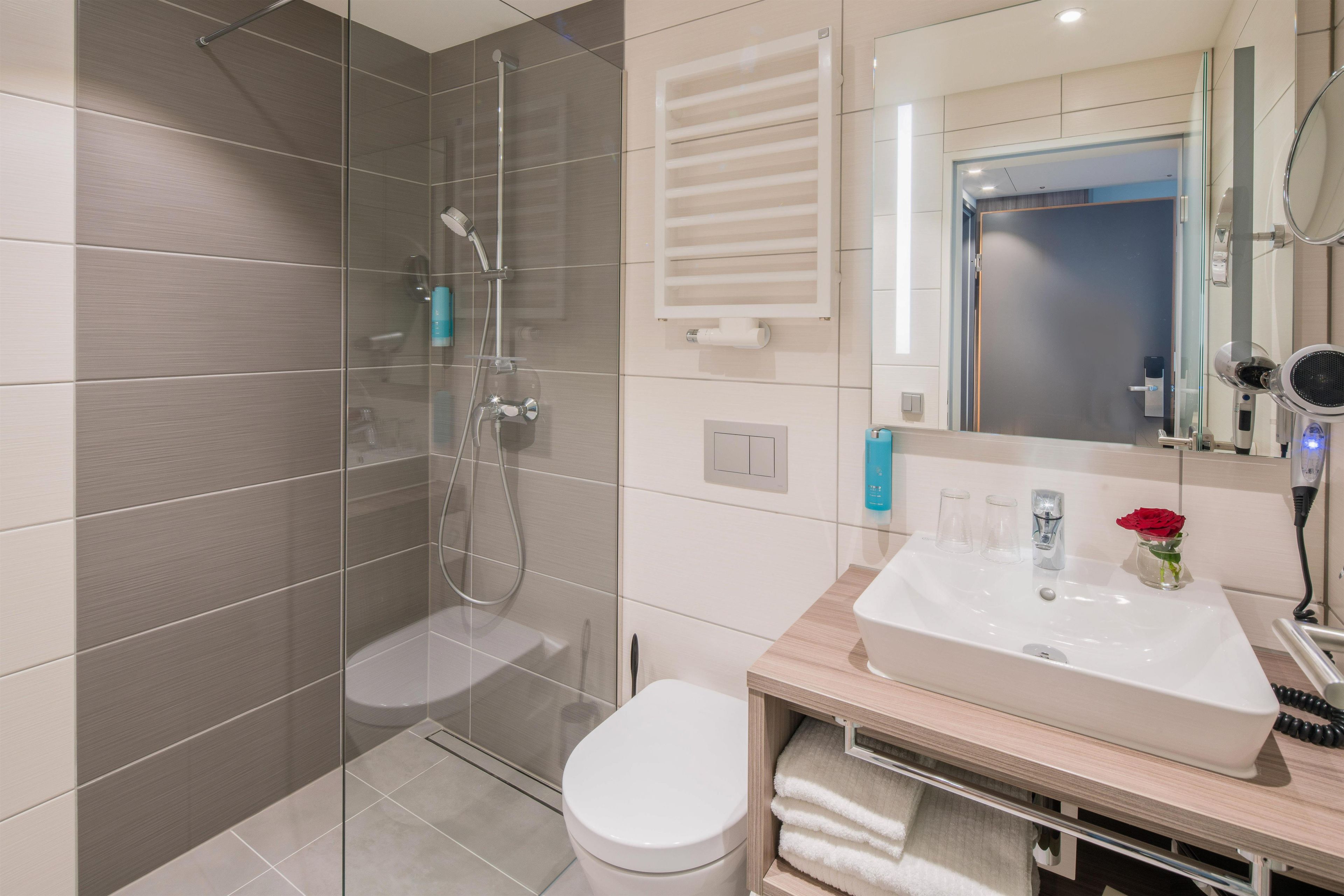 Ein modernes Badezimmer mit einer Duschkabine, einer weißen Toilette und einem Waschtisch mit Spüle und Spiegel.