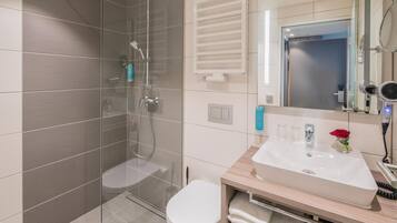 Ein modernes Badezimmer mit einer Duschkabine, einer weißen Toilette und einem Waschtisch mit Spüle und Spiegel.