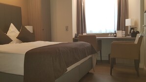 A hotel room with a bed, a desk, a chair, and a window with curtains. - Best Western Plus Hotel Regence (Aachen)
