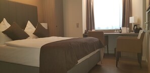 A hotel room with a bed, a desk, a chair, and a window with curtains. - Best Western Plus Hotel Regence (Aachen)