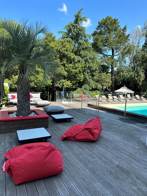 Un área junto a la piscina con sillones de descanso, una palmera y un pabellón.