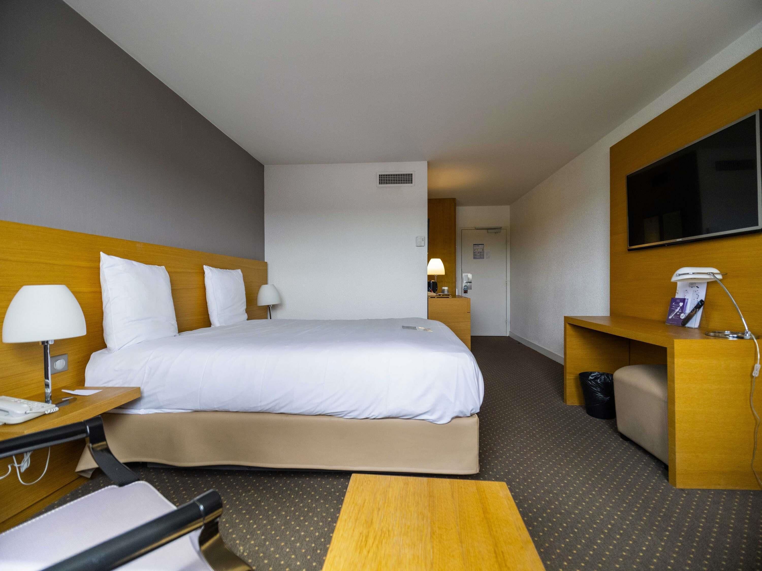 Habitación de hotel con cama, mesitas de noche, escritorio, silla, televisor y puerta al baño.