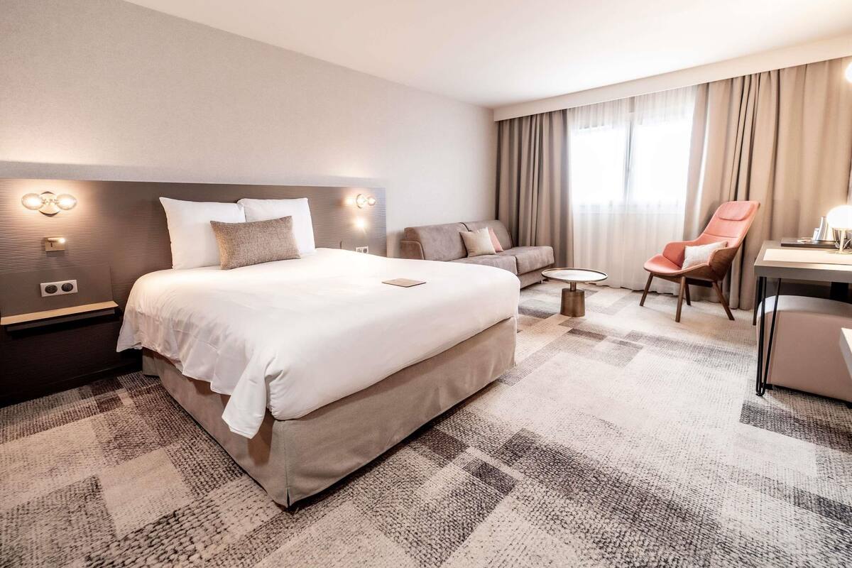 A hotel room with a large bed, a sofa, a chair, a small table, and a desk.