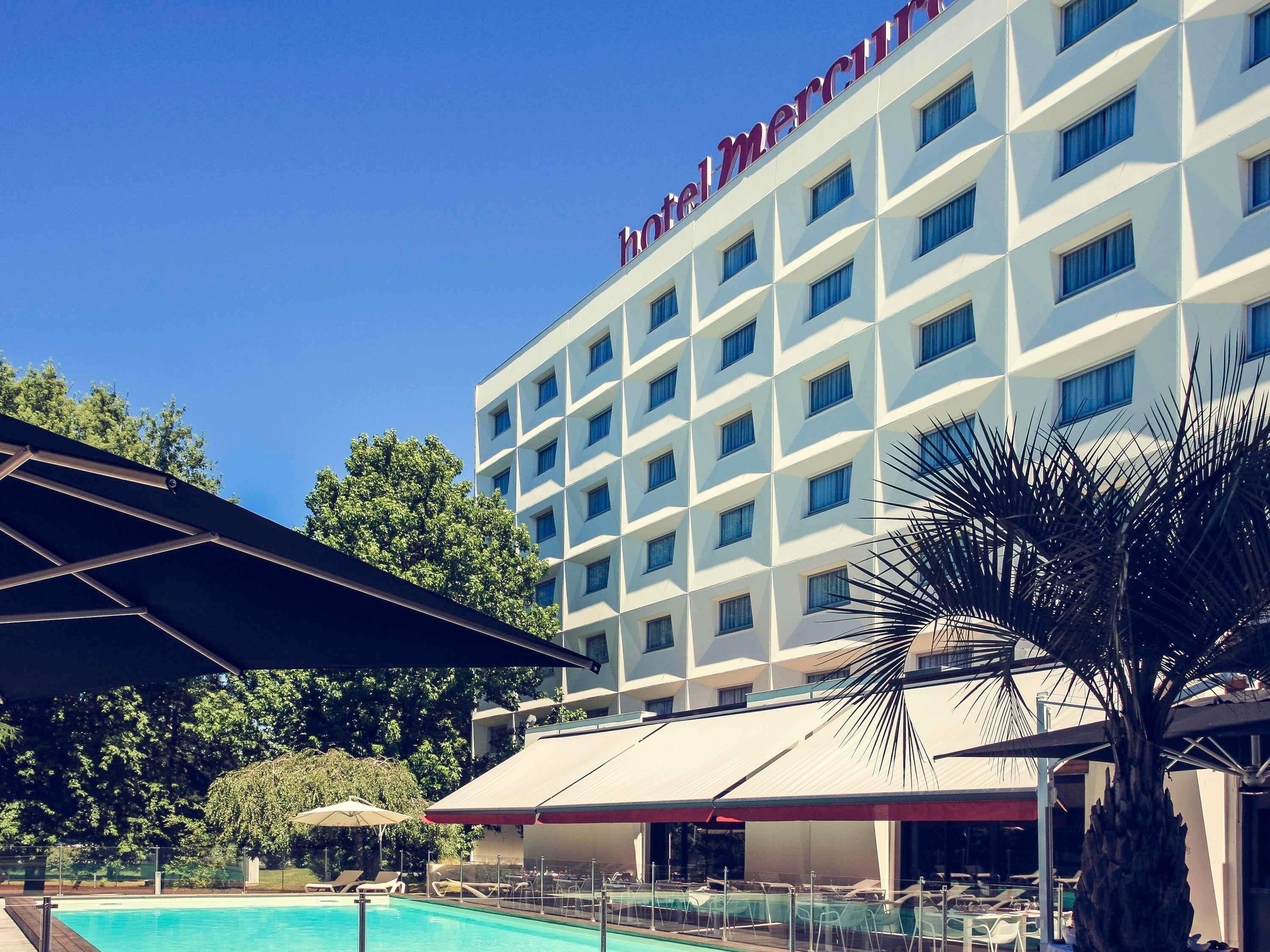 Een hotel met een zwembad, terras en een helderblauwe lucht.