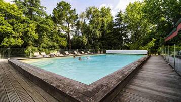 Una piscina rettangolare con un pontile in legno che la circonda, immersa nel verde degli alberi.