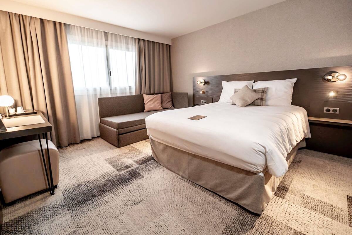 A hotel room with a bed, bedside table, lamp, and a sofa.