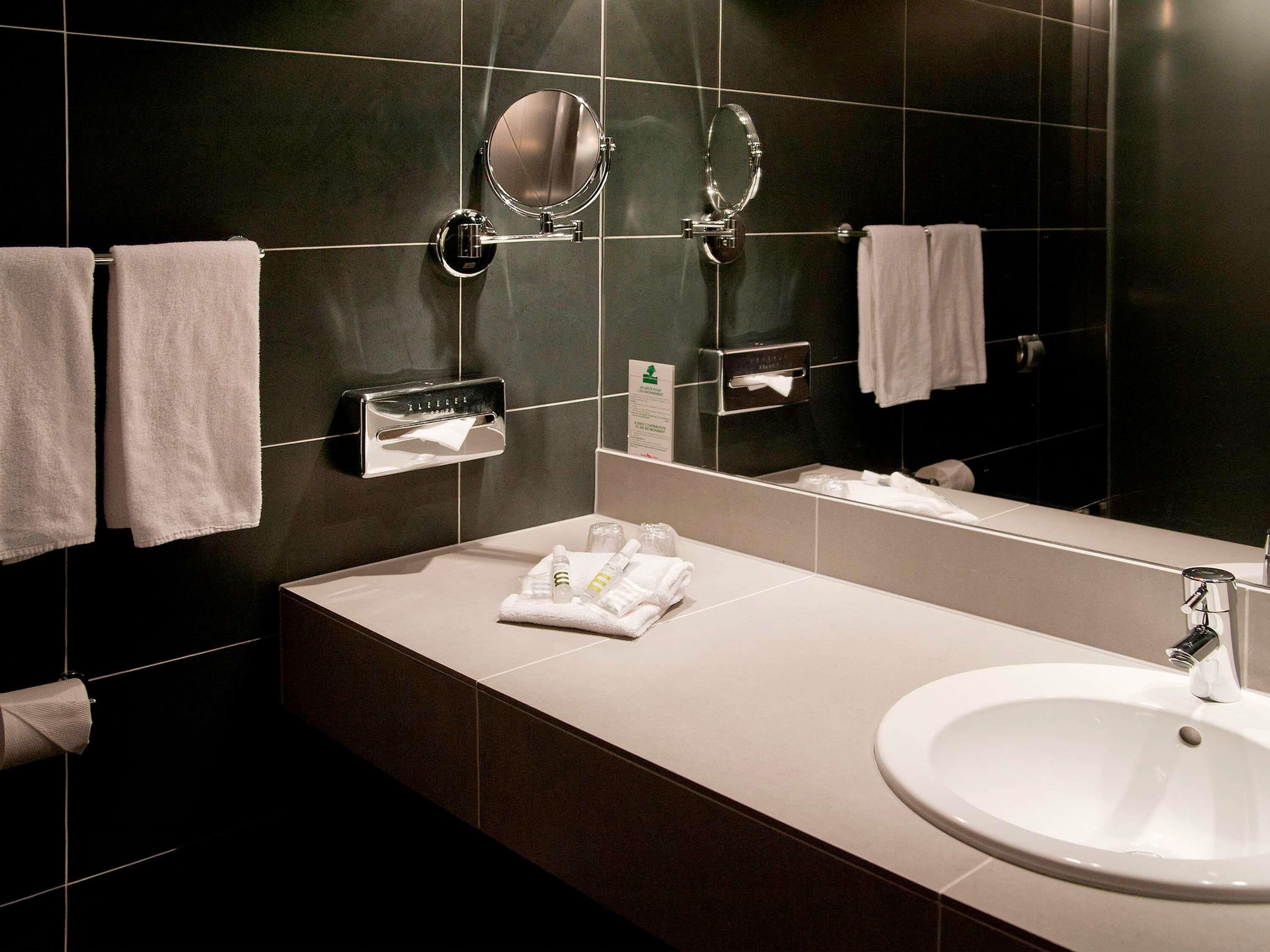 Un baño moderno con un espejo grande, dos toalleros, un lavamanos y un dispensador de pañuelos.