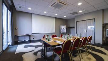 Una sala de conferencias con una pantalla grande, un proyector, una mesa con sillas y una alfombra estampada.