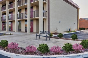 A multi-story building with a brick facade, a parking lot, and a bench in the foreground.