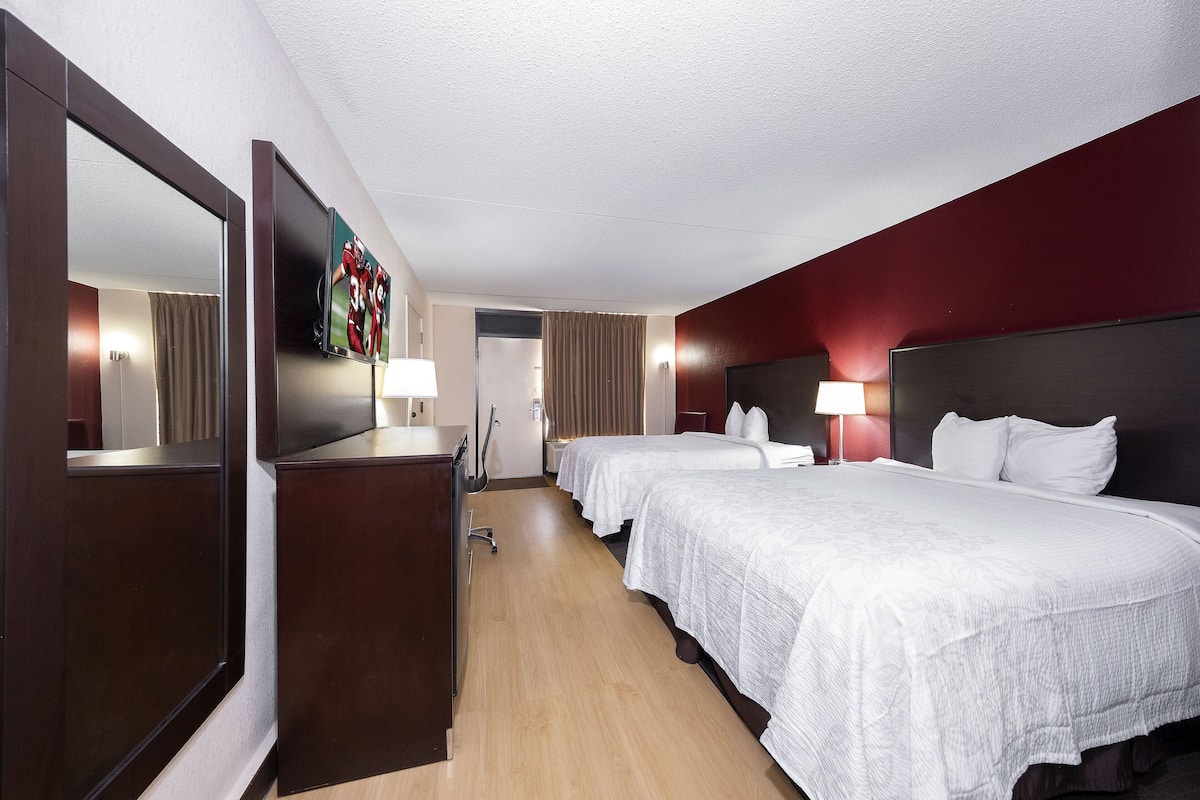 Une chambre d’hôtel avec deux lits, un grand miroir, un téléviseur fixé au mur et un bureau avec une lampe.