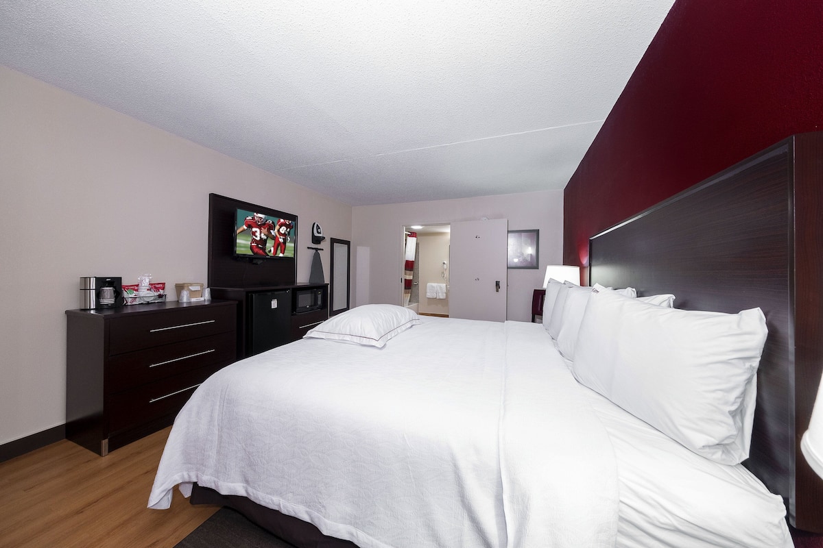 Une chambre d’hôtel avec un grand lit, un téléviseur posé sur une commode, une machine à café et une porte donnant sur une autre pièce.