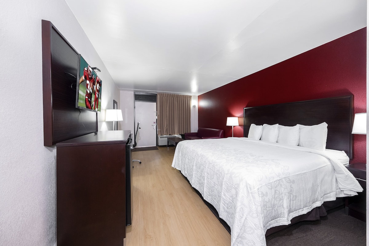 Une chambre d’hôtel avec un grand lit, un bureau avec une chaise, un téléviseur fixé au mur et un mur d’accent de couleur rouge.