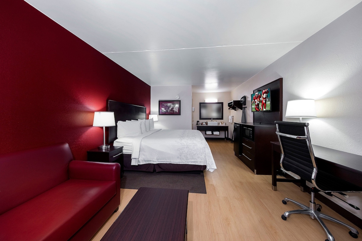 A hotel room with a bed, a desk, a chair, a TV, and a red wall.