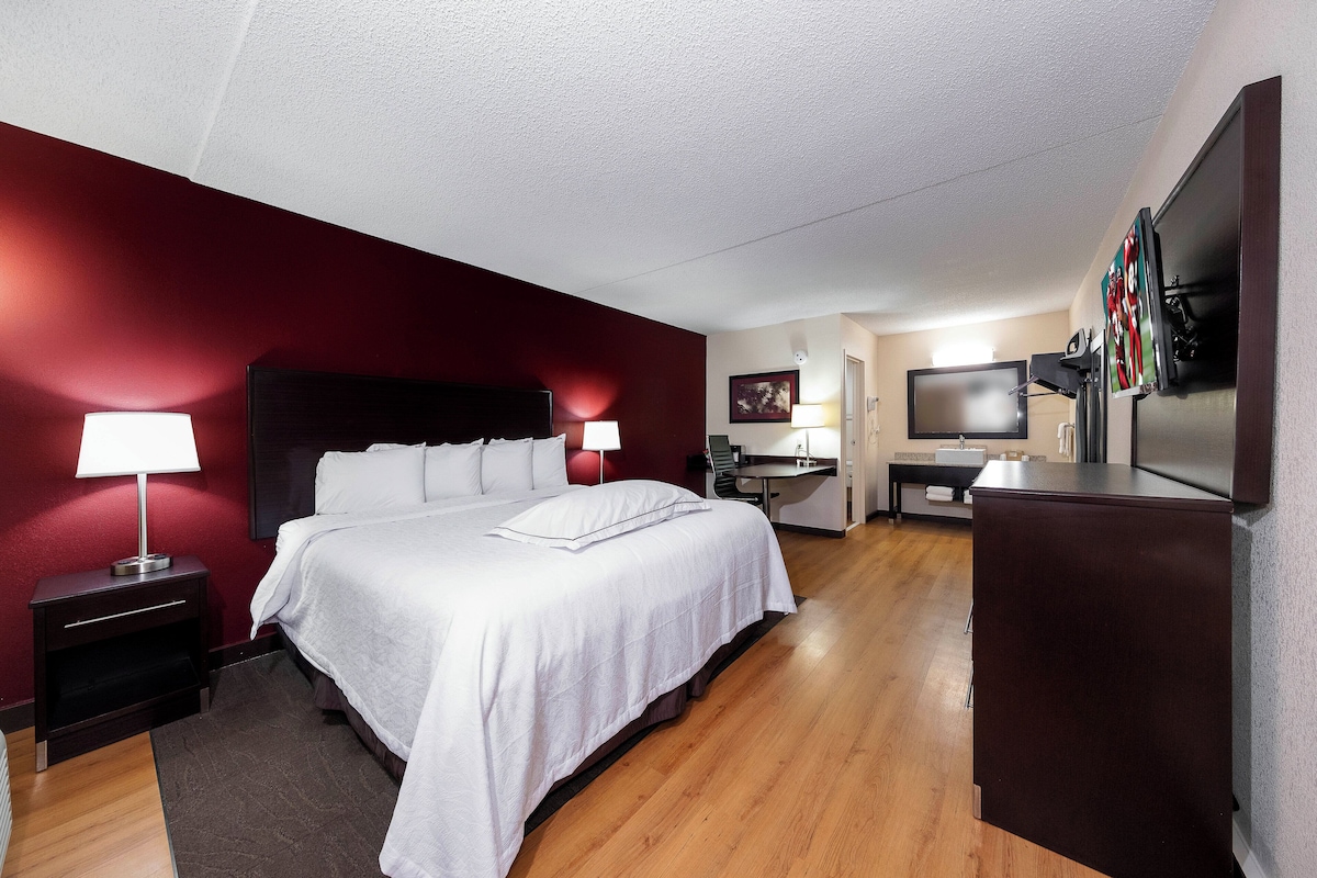 A hotel room with a bed, bedside lamps, a desk, a television, and a mirror.