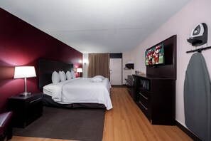 A hotel room with a bed, a desk, a TV, a mirror, and a wardrobe. - Red Roof Inn PLUS+ Huntsville - Madison (Madison)
