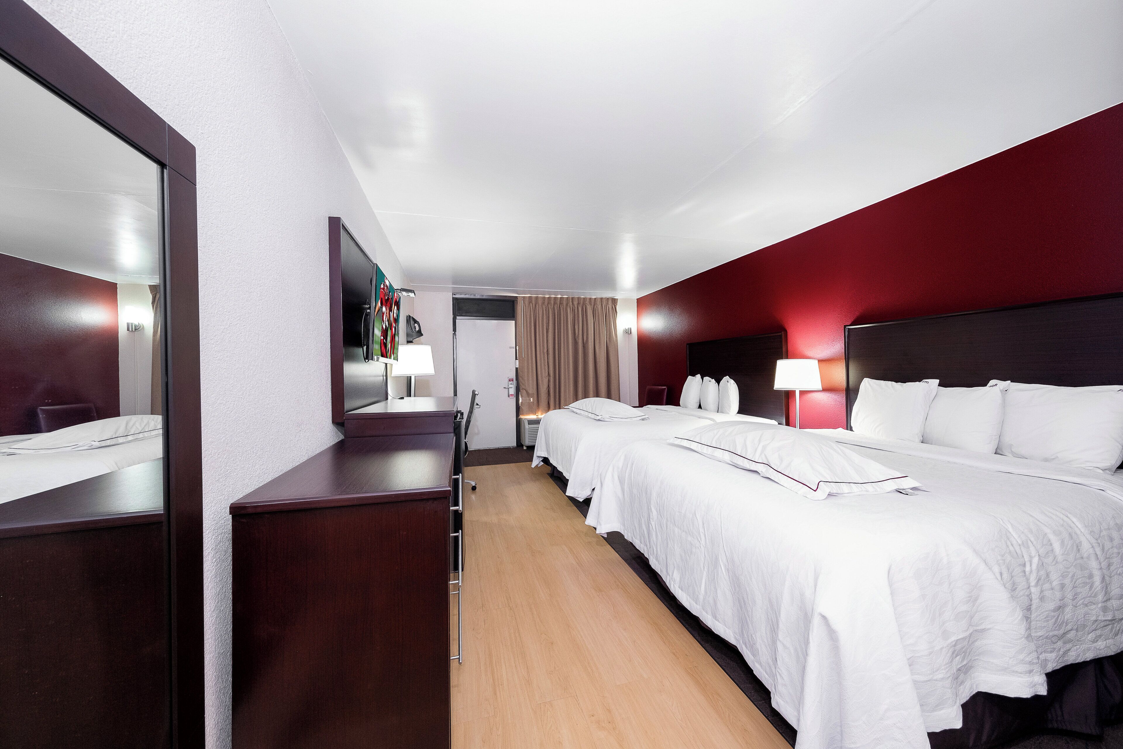 Una habitación de hotel con dos camas, un escritorio, un espejo y un armario.