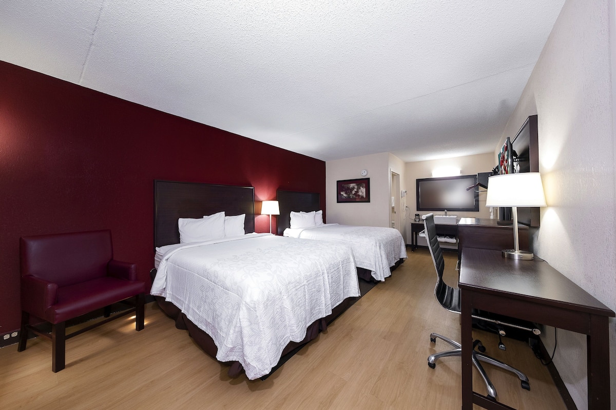 Une chambre d’hôtel avec deux lits, un bureau, une chaise et un téléviseur.