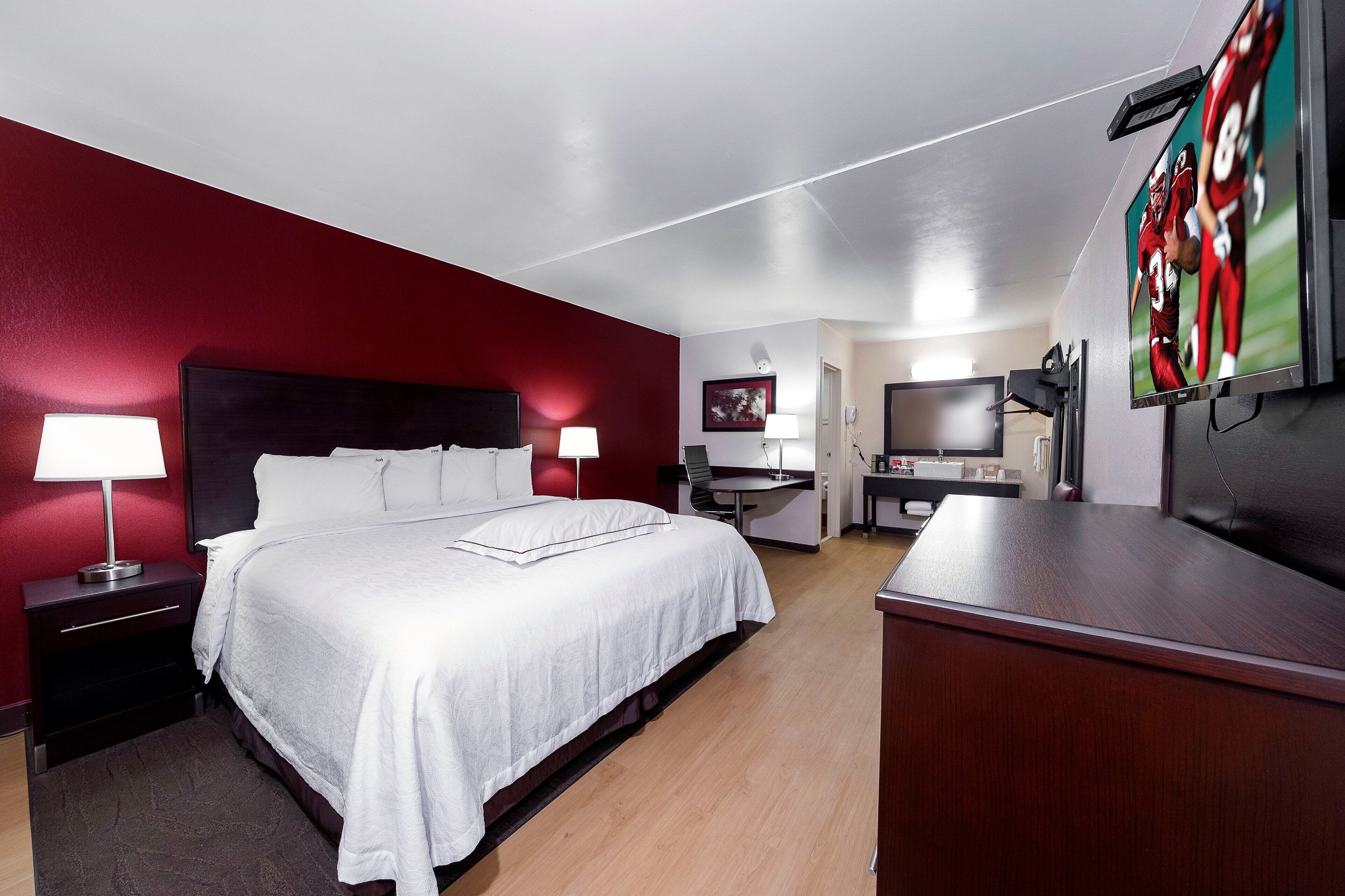 A hotel room with a bed, bedside tables, a desk, a television, and a mirror.