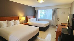 Habitación de hotel con dos camas, un escritorio con televisor y un ventanal con cortinas.