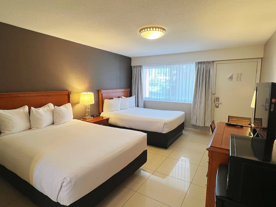Habitación de hotel con dos camas, un escritorio con televisor y un ventanal con cortinas.