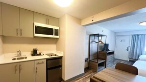 Una habitación de hotel pequeña con kitchenette, comedor y cama.