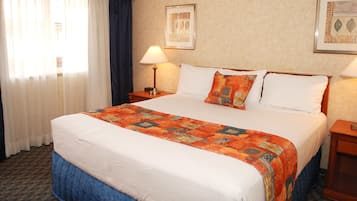 A hotel room with a large bed, two bedside tables, a window with curtains, and two framed pictures on the wall.