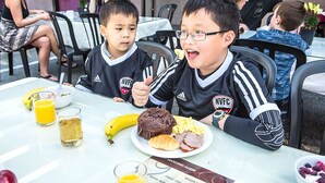 Una mesa de comedor con comida y bebidas, un menú, y un grupo de personas sentadas.