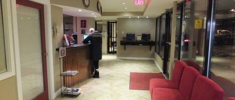 Un hall d’hôtel avec un comptoir d’accueil, un canapé rouge et une porte vitrée donnant sur l’extérieur.