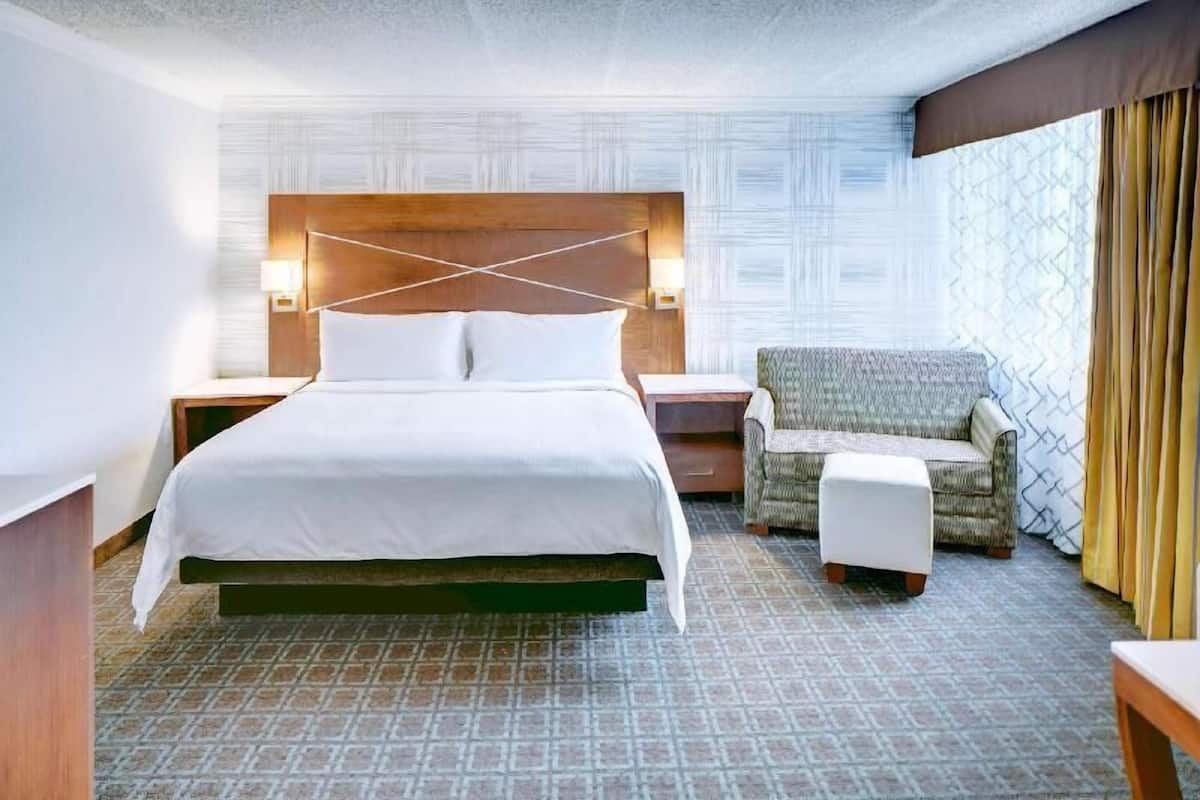 A hotel room with a large bed, a chair, a nightstand, and a patterned wall.