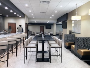 A modern dining area with a long table and multiple chairs, a bar area with stools, and a seating section with cushioned booths. - DoubleTree by Hilton Madison Downtown (Madison)