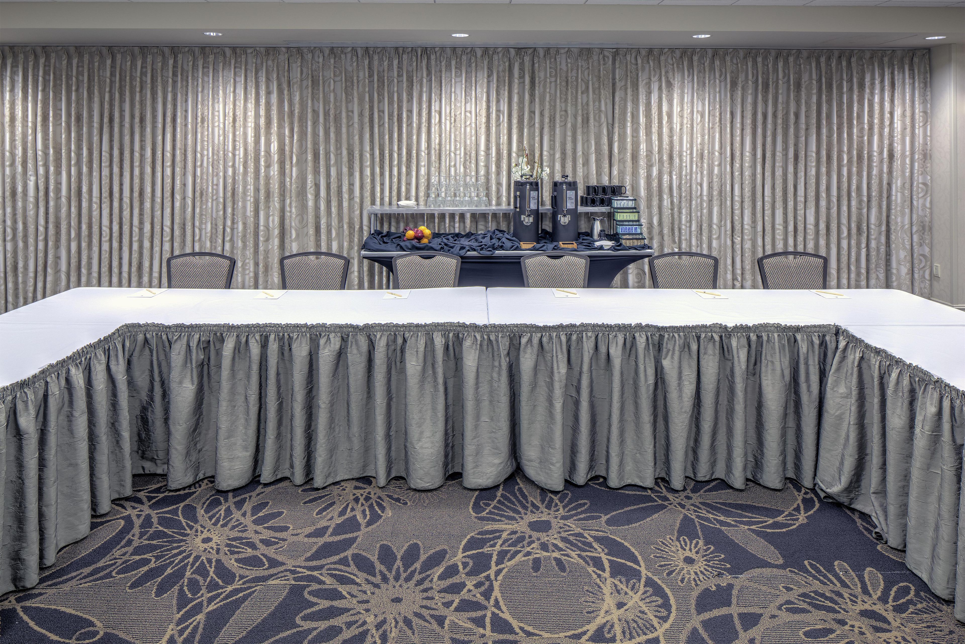 A conference room with a long table, chairs, a coffee station, and a patterned carpet.