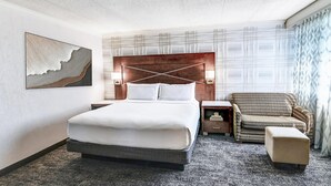 A hotel room with a large bed, a nightstand, a chair, and a wall-mounted lamp.