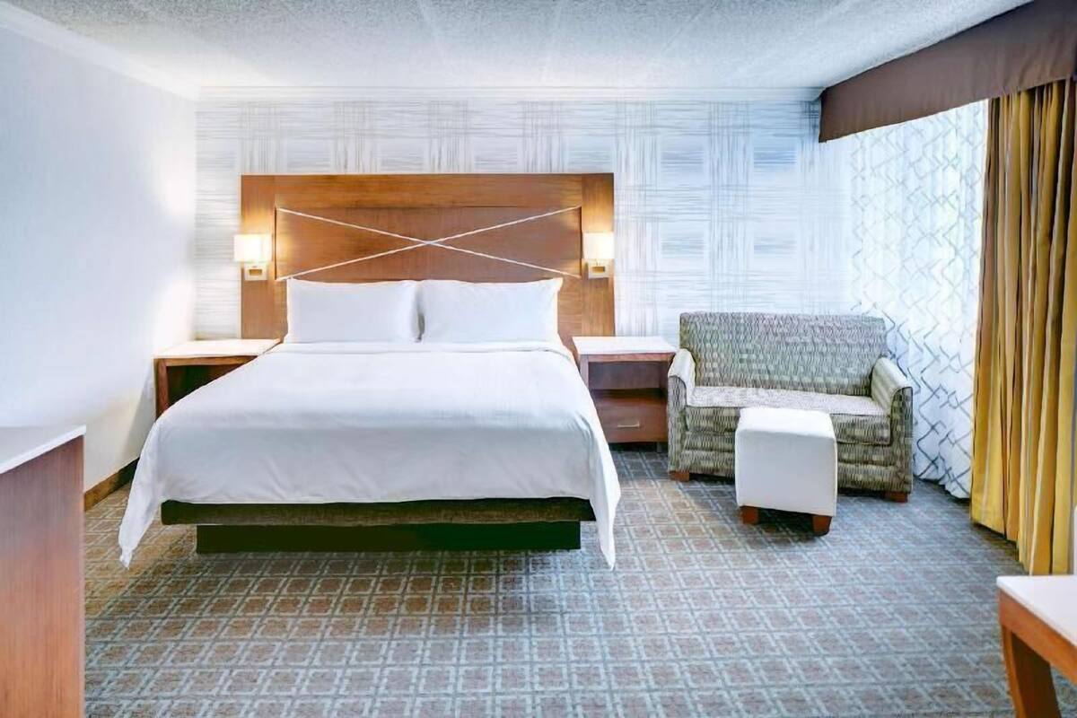 A hotel room with a large bed, a chair, a nightstand, and a patterned wall.