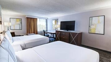 A hotel room with two beds, a desk, a TV, and artwork on the walls.