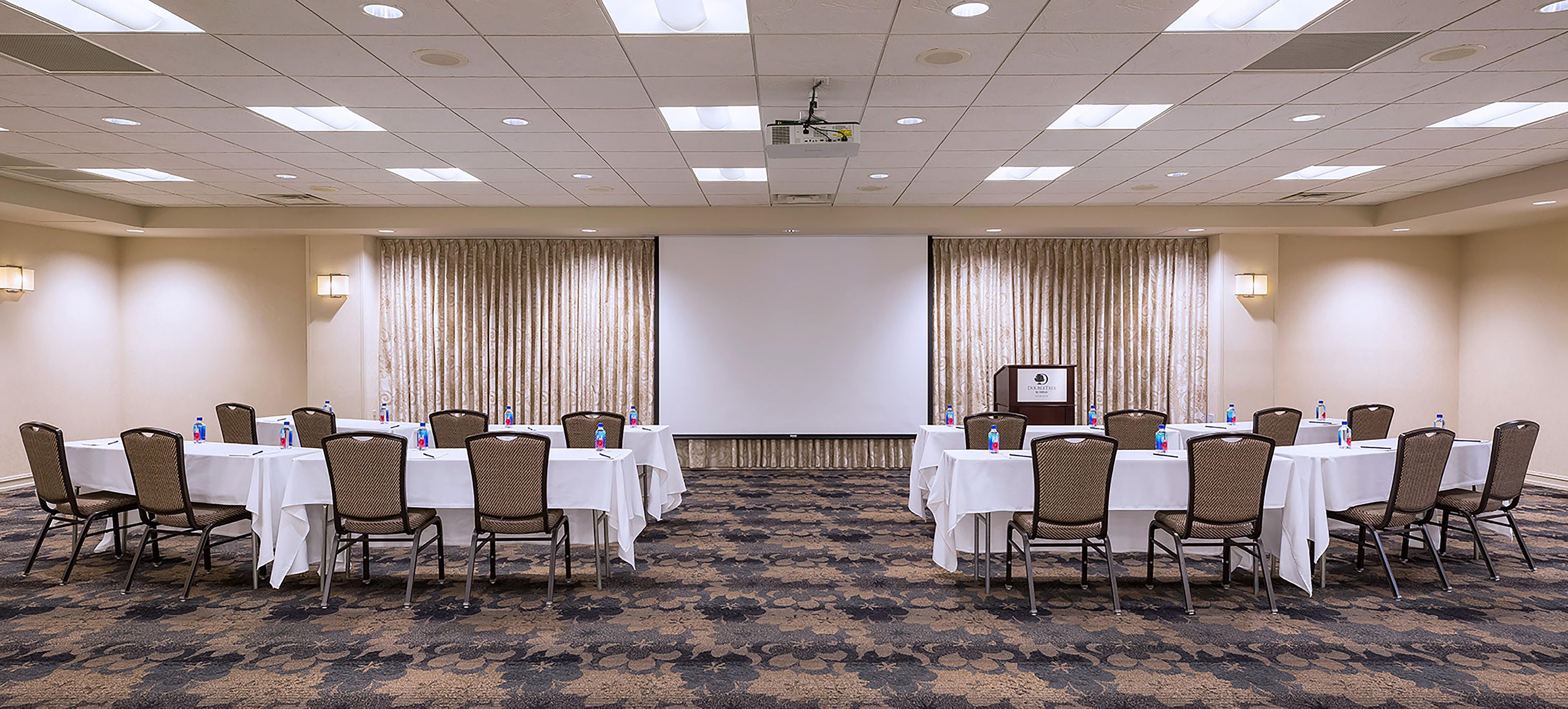 A conference room with tables and chairs, a projector, and curtains.