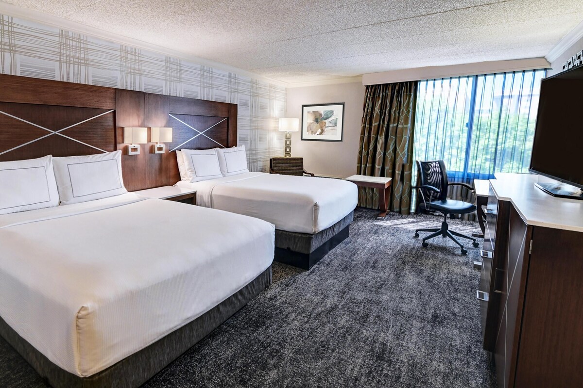 A hotel room with two beds, a desk, a chair, and a window with curtains.