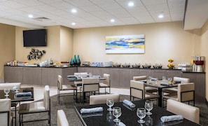 Un comedor de hotel con varias mesas y sillas, una barra de buffet y un televisor de pantalla plana montado en la pared.