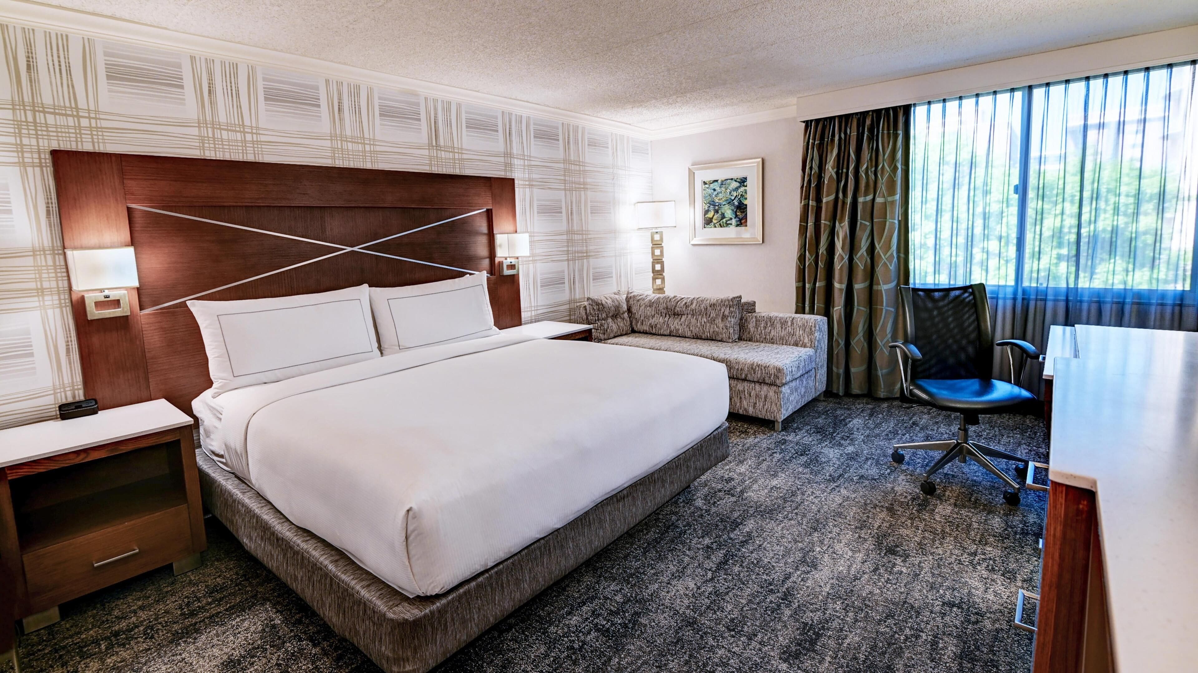 A hotel room with a large bed, a sofa, a desk, and a chair.