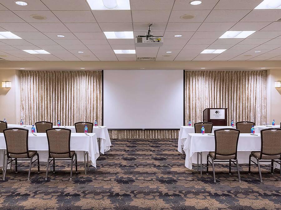 A conference room with tables and chairs, a projector screen, and curtains.